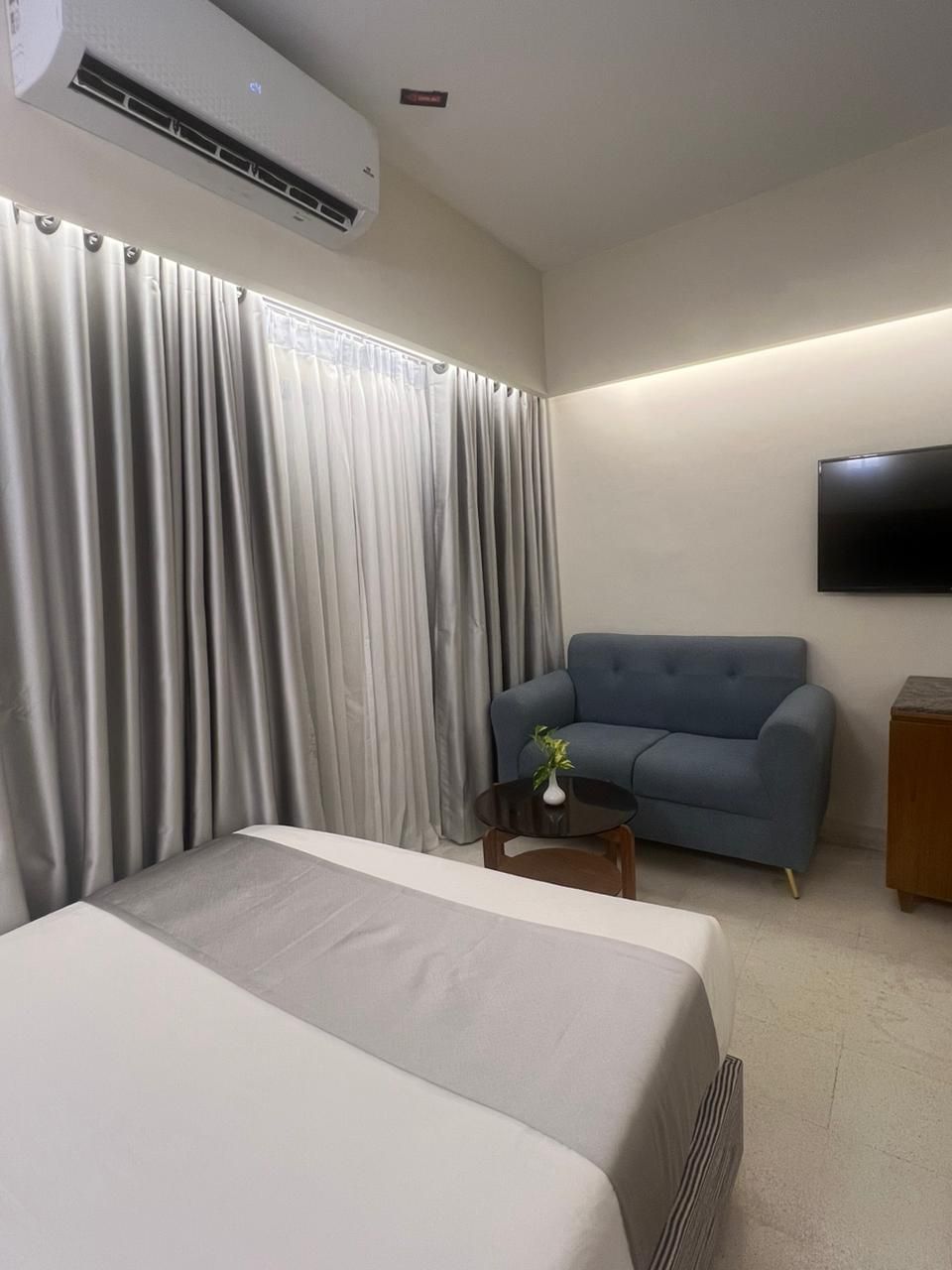 A hotel room with a bed, a blue sofa, a small table with a plant, and a mounted TV.