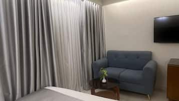 A hotel room with a bed, a blue sofa, a small table with a plant, and a mounted TV.