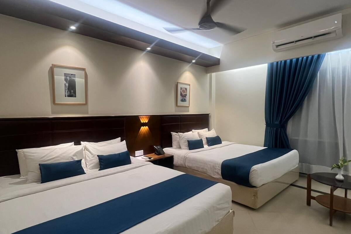 Habitació d'hotel amb dos llits, una taula de nit, una làmpada i una finestra amb cortines.