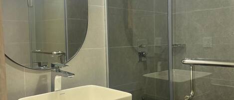 A modern bathroom with a white sink, a large mirror, and a glass shower enclosure.
