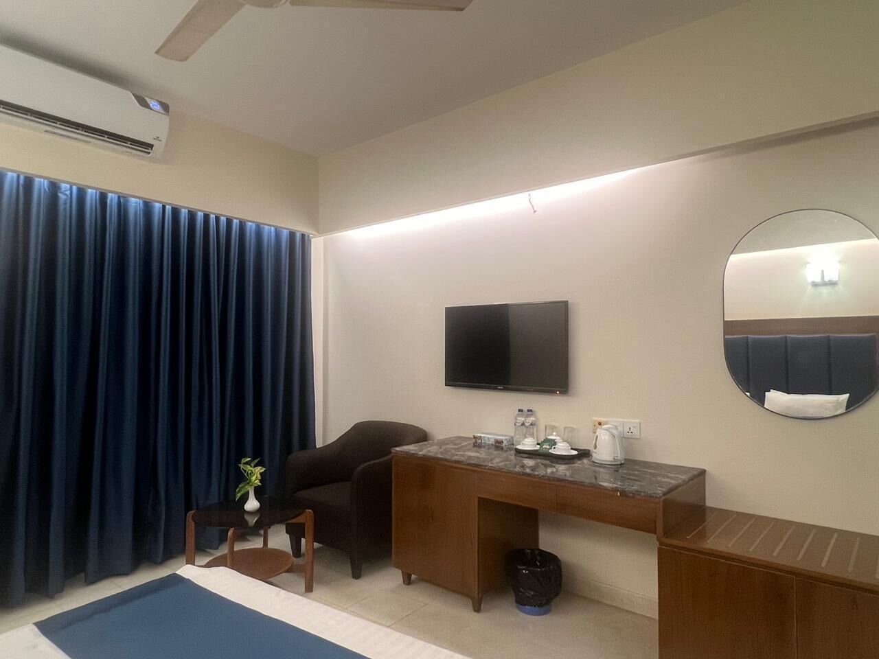 A hotel room with a desk, chair, television, and a large mirror.