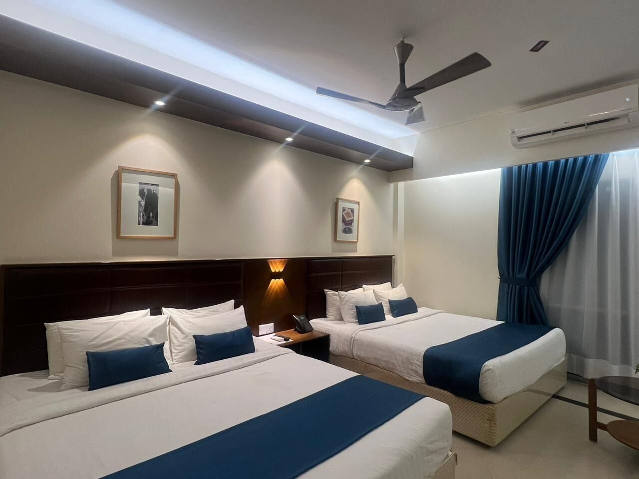 Habitación de hotel con dos camas, una mesita de noche, un ventilador de techo y un equipo de aire acondicionado.