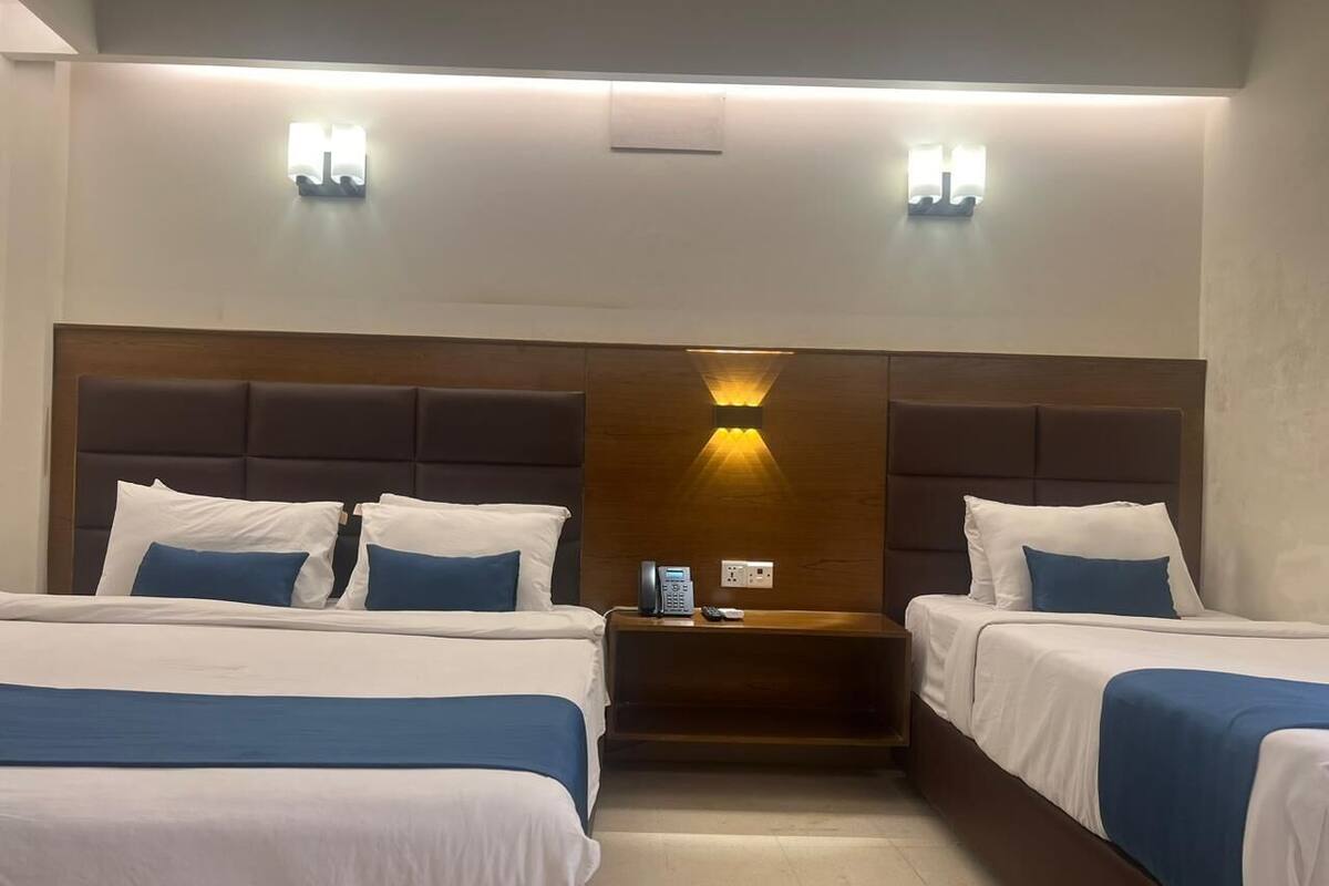 Habitació d'hotel amb dos llits, un panell de capçalera de fusta, una tauleta de nit amb un telèfon i llums penjades a la paret.