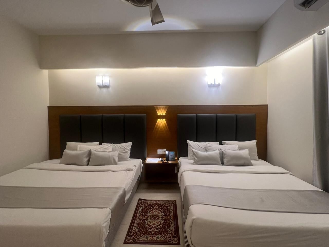 Una camera d'albergo con due letti, un comodino e una lampada a parete.