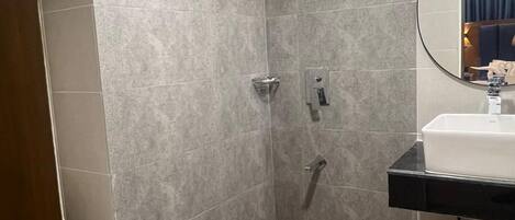 A bathroom with grey tiles, a wooden floor, a white toilet, a sink with a mirror, and a shower.