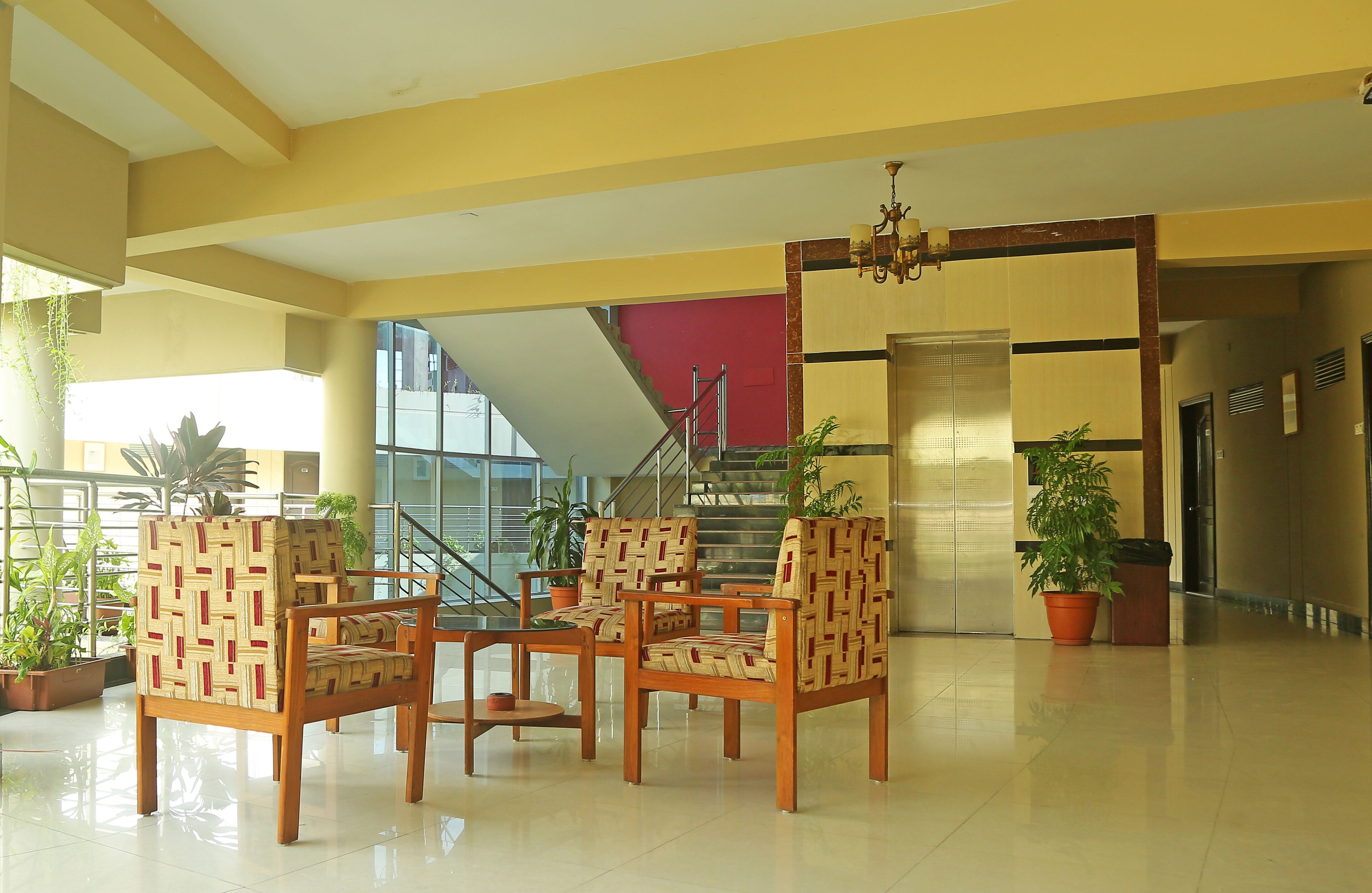 A spacious lobby with a staircase, wooden chairs, and potted plants.