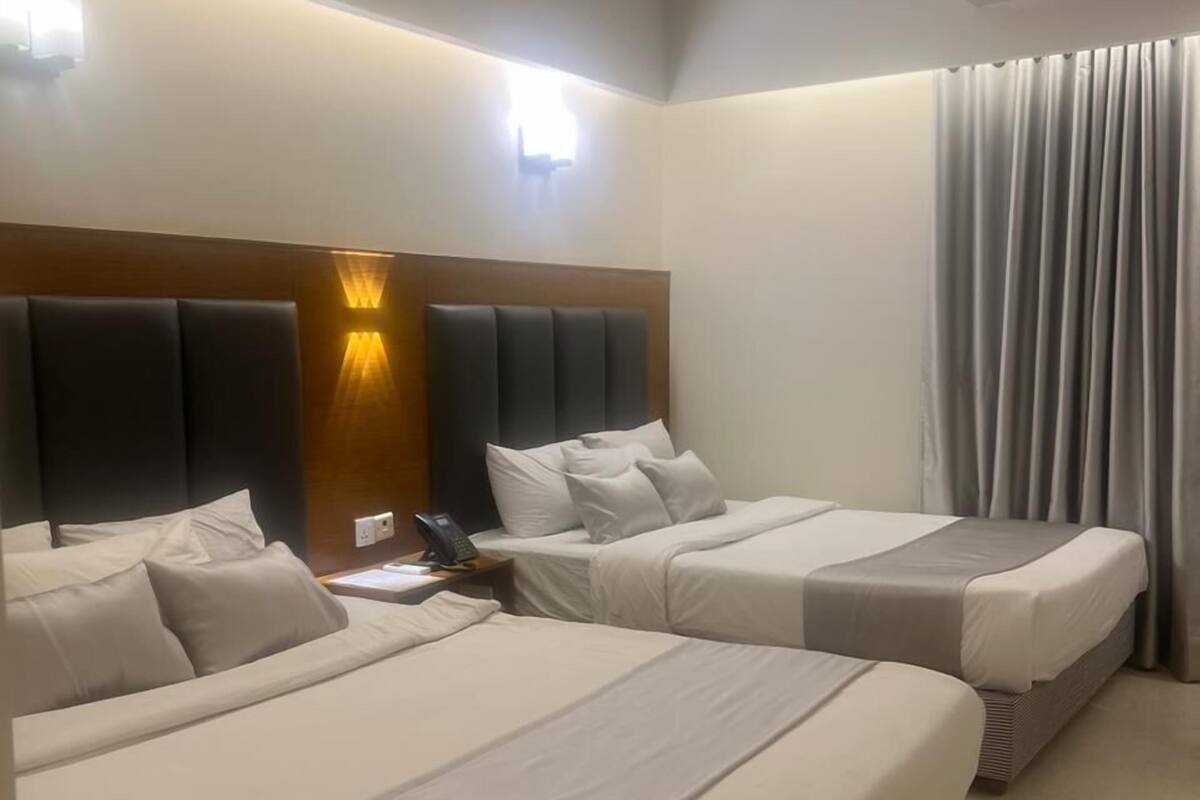 Una habitació d'hotel amb dos llits, un ventilador de sostre, un aparell d'aire condicionat i una finestra amb cortines.