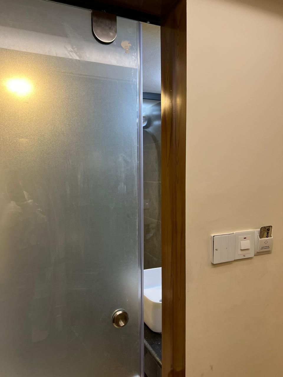 Ein Badezimmer mit einer Metalltür, einem weißen Waschbecken und einem Lichtschalter an der Wand.