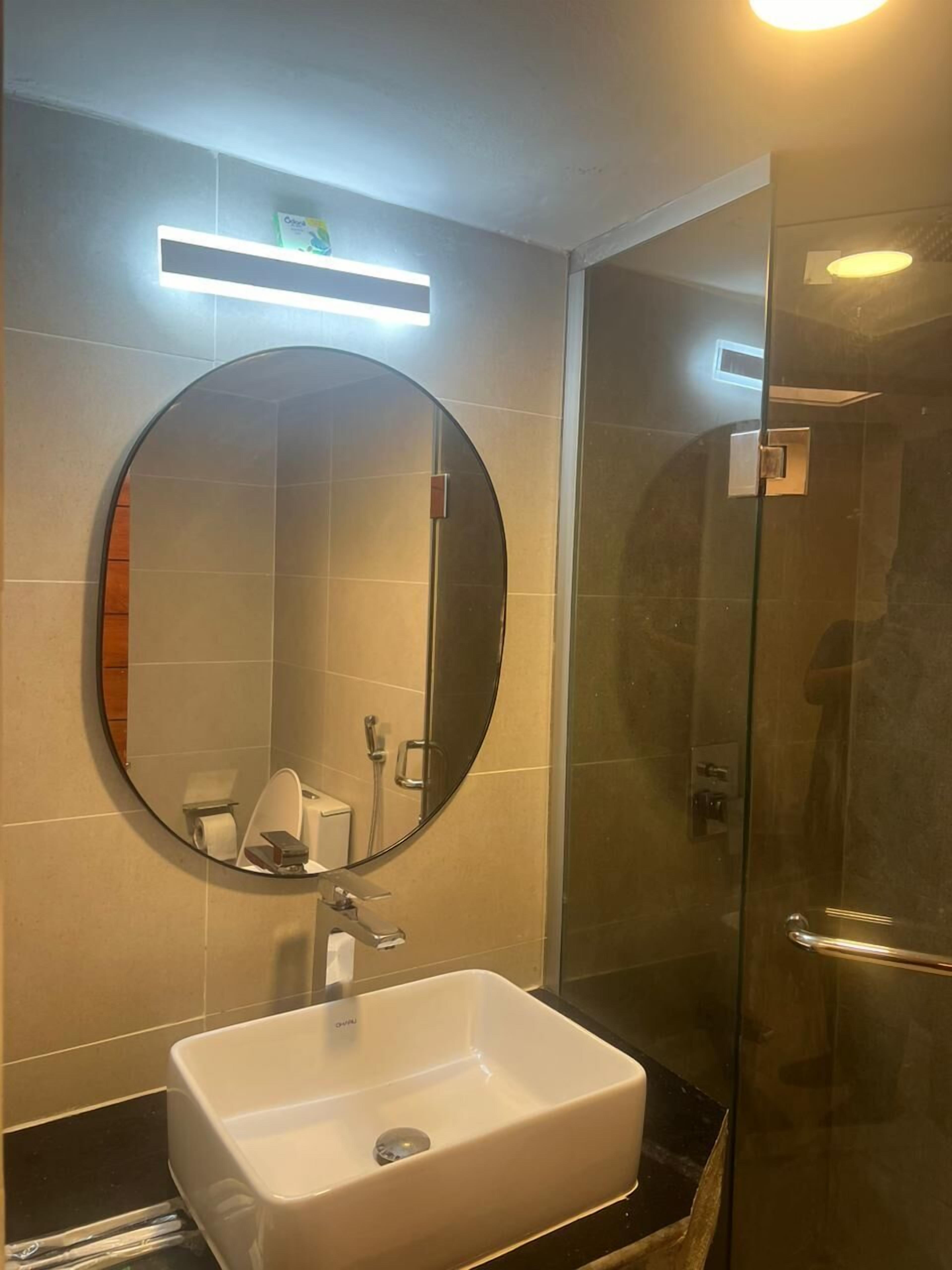 A bathroom with a round mirror, a rectangular sink, and a glass shower enclosure.