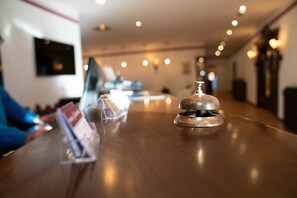 A wooden reception desk with a bell, a glass display case, and a television mounted on the wall. - Hotel Löwenstein (Gerolstein)