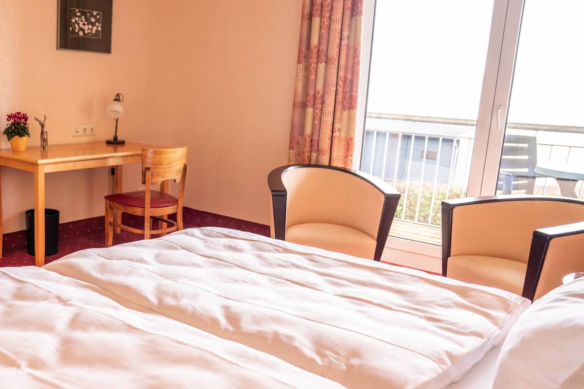Habitación de hotel con una cama grande, un escritorio, dos sillas y un balcón con vistas.