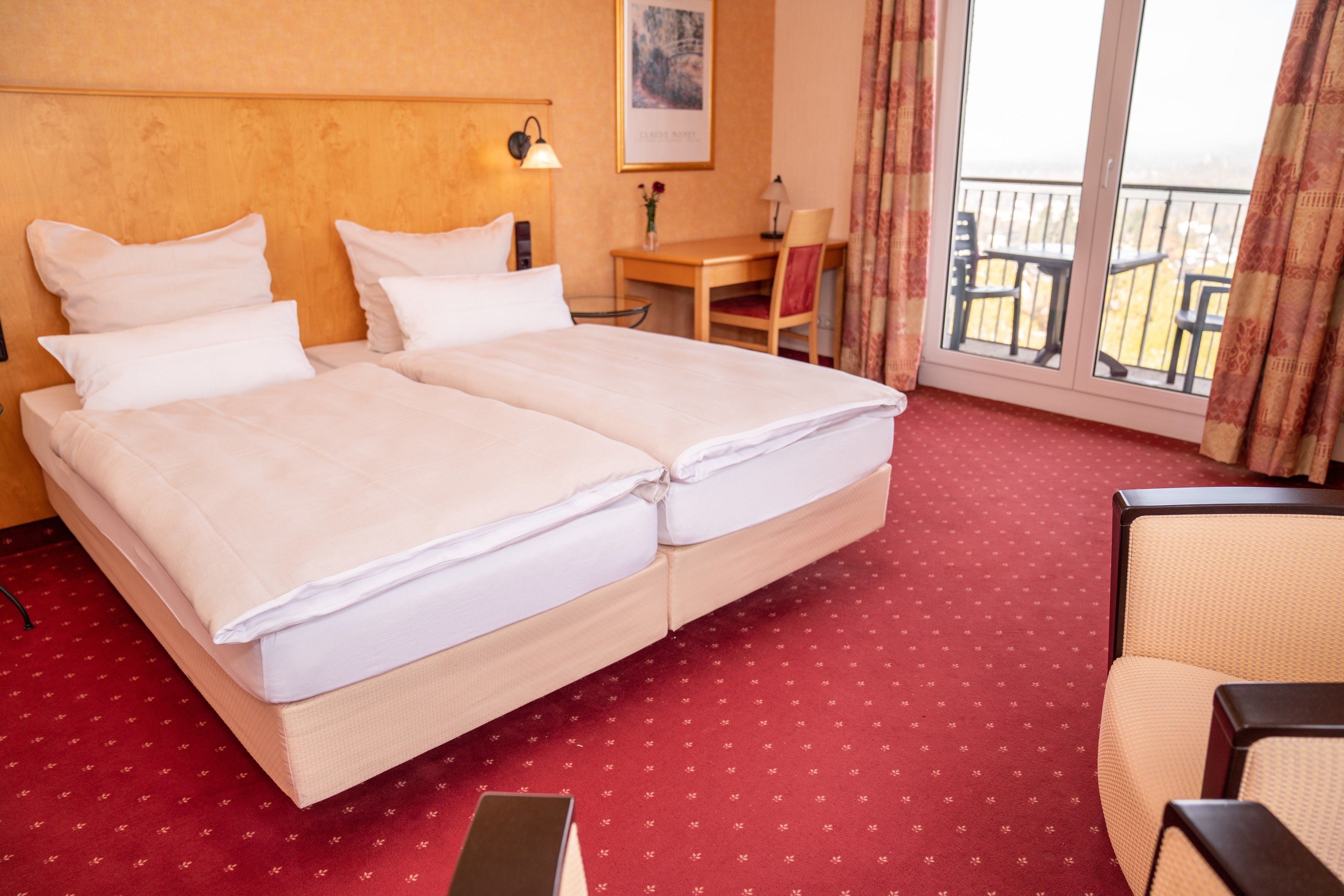 A hotel room with a double bed, a desk, a chair, and a balcony with outdoor seating.