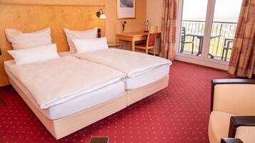 A hotel room with a double bed, a desk, a chair, and a balcony with outdoor seating.