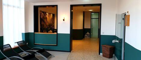 A reception area with a reception desk, chairs, a wall-mounted mirror, and a door leading to a hallway.