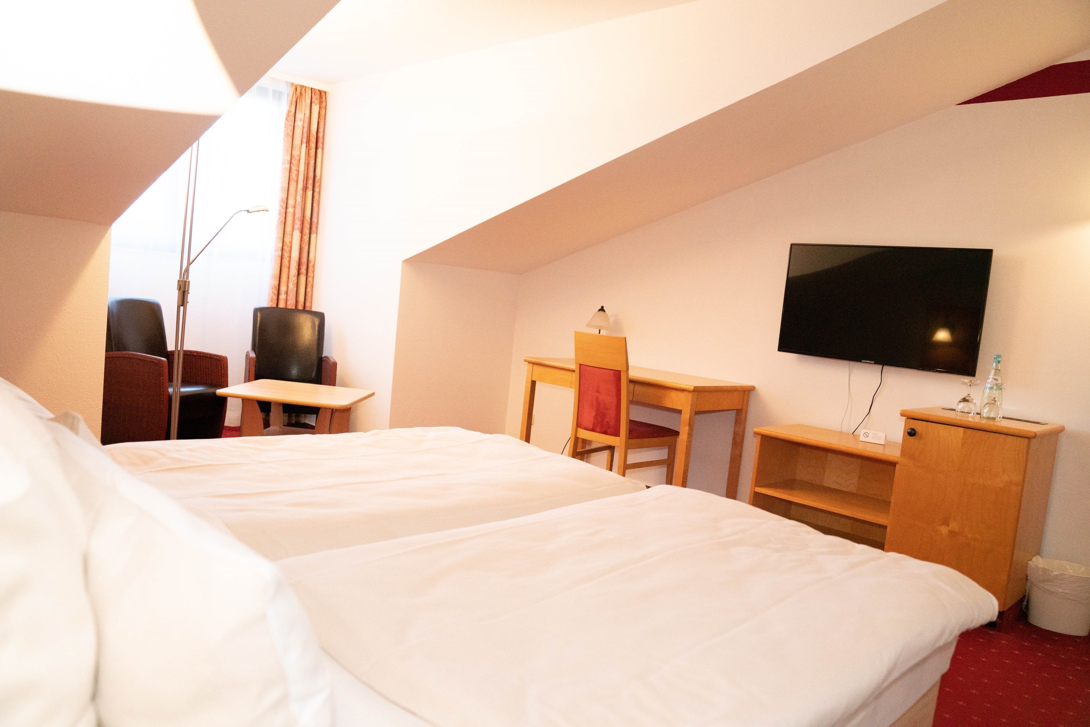 A hotel room with two beds, a desk, a chair, a television, and a small cabinet.