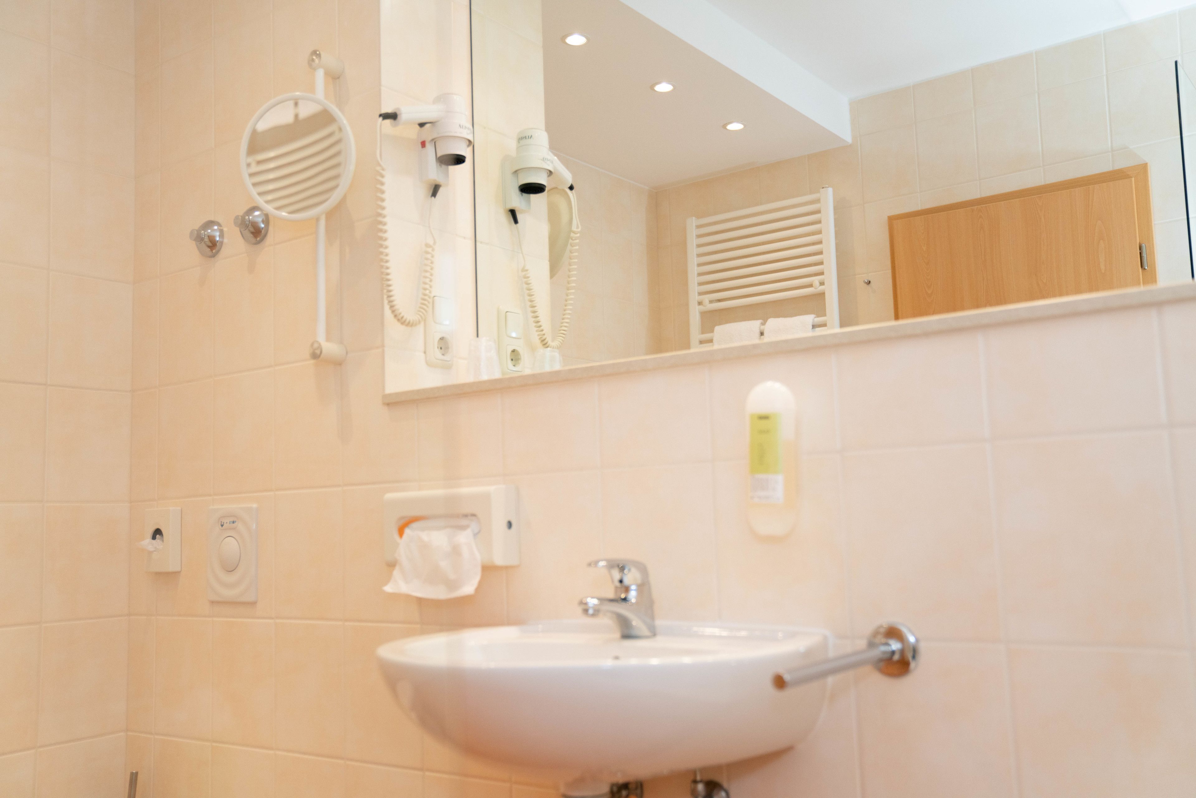 A bathroom with a sink, mirror, hairdryer, and towel rack.