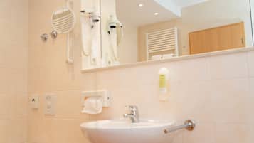 Une salle de bain équipée d’un lavabo, d’un miroir, d’un sèche-cheveux et d’un porte-serviettes.