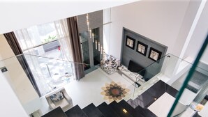 Un interior moderno con una escalera de cristal, una alfombra estampada y un área de descanso con sofá y mesa de centro.