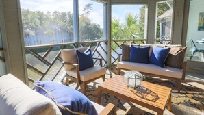 A sunlit room with a view of a lake, furnished with a sofa, chairs, and a coffee table. - Short Walk to Beach. Dog-Friendly, Renovated, Bright & Modern Villa with Lagoon Views. (Kiawah Island)
