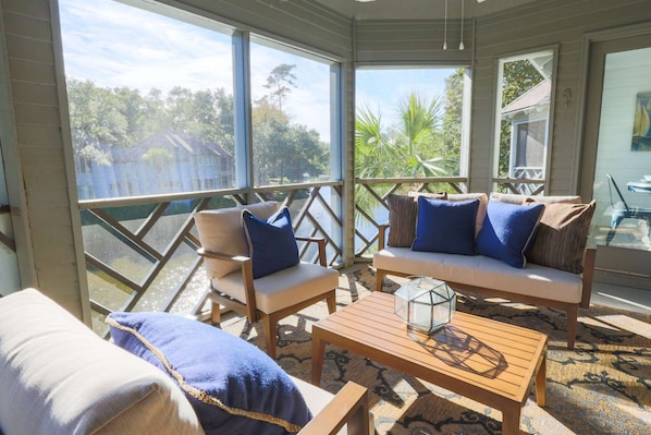 A sunlit room with a view of a lake, furnished with a sofa, chairs, and a coffee table. - Short Walk to Beach. Dog-Friendly, Renovated, Bright & Modern Villa with Lagoon Views. (Kiawah Island)