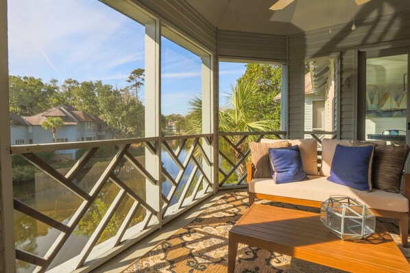 A balcony with a sofa and table, large windows, and a view of houses and trees.