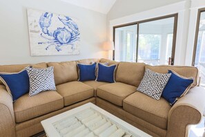A beige sectional sofa with blue and patterned cushions, a white coffee table, and a large blue and white artwork on the wall.