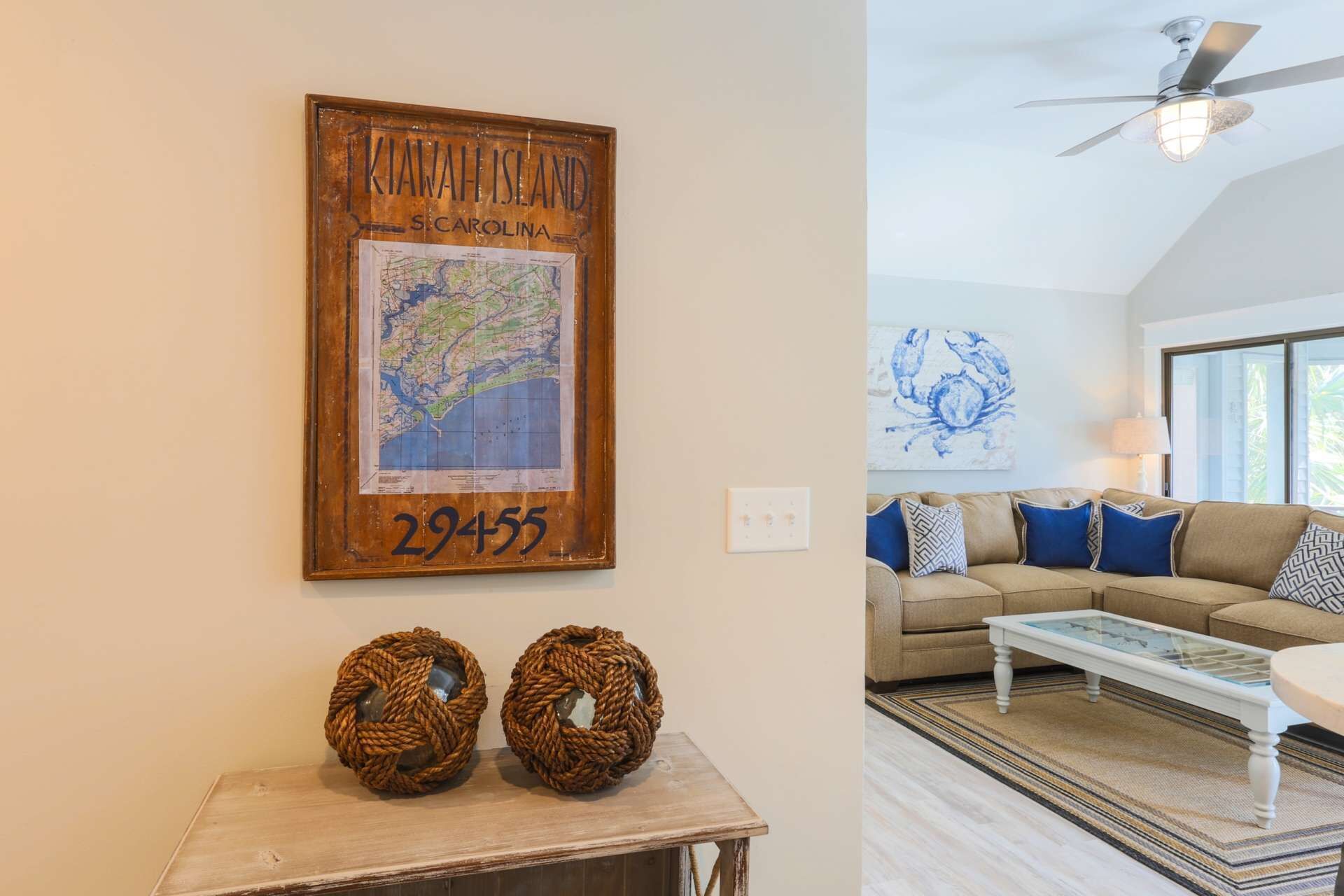 A living room with a large window, a ceiling fan, a map of Kiawah Island, and two woven baskets on a table.