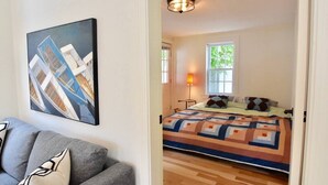 Une chambre à coucher avec un lit, une table de chevet, une lampe, une fenêtre et un tableau au mur.