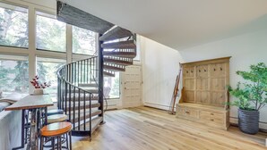 Quarto amplo com escada em espiral, piso de madeira, um banco e uma grande janela.