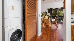 Un área de lavandería con lavadora, una puerta corredera de madera, y un comedor con mesa y sillas.