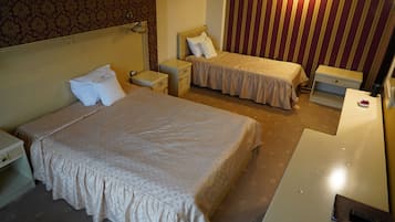 Une chambre d’hôtel avec deux lits, une table de chevet, une lampe, un radiateur et une petite table sur laquelle se trouve un bol de fruits.