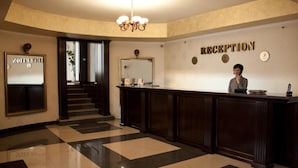 A reception area with a check-in counter, a staircase, and a wall-mounted clock. - Hotel Majestic (Iasi)