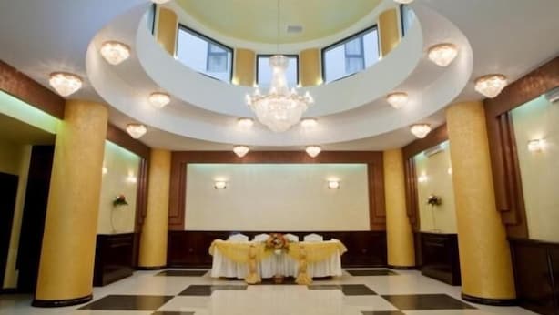 A spacious hall with a high ceiling, chandeliers, and a central table with a floral arrangement. - Hotel Majestic (Iasi)