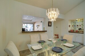 A dining area with a glass table, chairs, and a chandelier. There is a kitchen area with a countertop and cabinets visible in the background. - 4 Mi to Dtwn Palm Springs: Condo w/ Pool Access (Cathedral City)