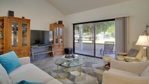 Ein Wohnzimmer mit einem Glastisch, weißen Sofas, einem Holzschrank und einem Fernseher.