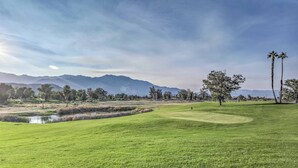 Ein Golfplatz mit Teich, Bäumen und Bergen im Hintergrund.