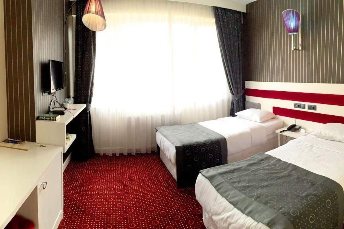 A hotel room with two beds, a desk, a TV, and a window with curtains.