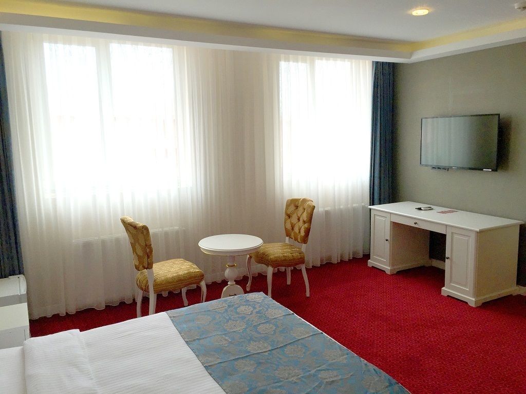 Ett hotellrum med en säng, två stolar, ett litet bord, ett skrivbord och en tv på väggen.
