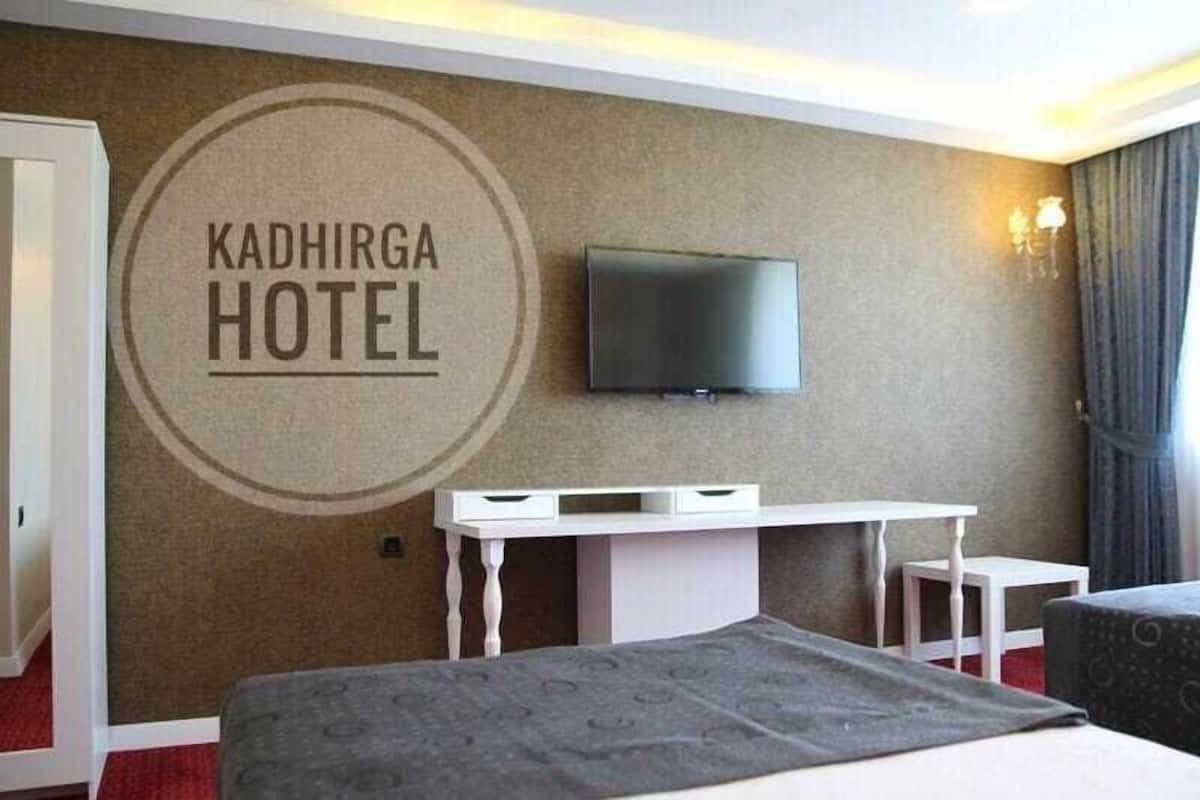 A hotel room with a bed, a TV mounted on the wall, a desk, and a small table.