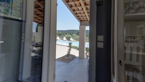 Une porte ouverte donne sur un espace extérieur abrité, équipé d’une piscine, de chaises longues et offrant une vue sur les collines.