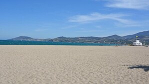 Une plage avec un bâtiment blanc et des montagnes en arrière-plan.