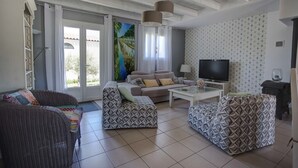 Un salon avec un canapé, un pouf, une télévision et un tableau accroché au mur.