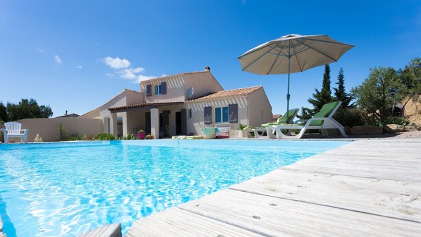 Une piscine avec une terrasse en bois, des chaises longues et un parasol.