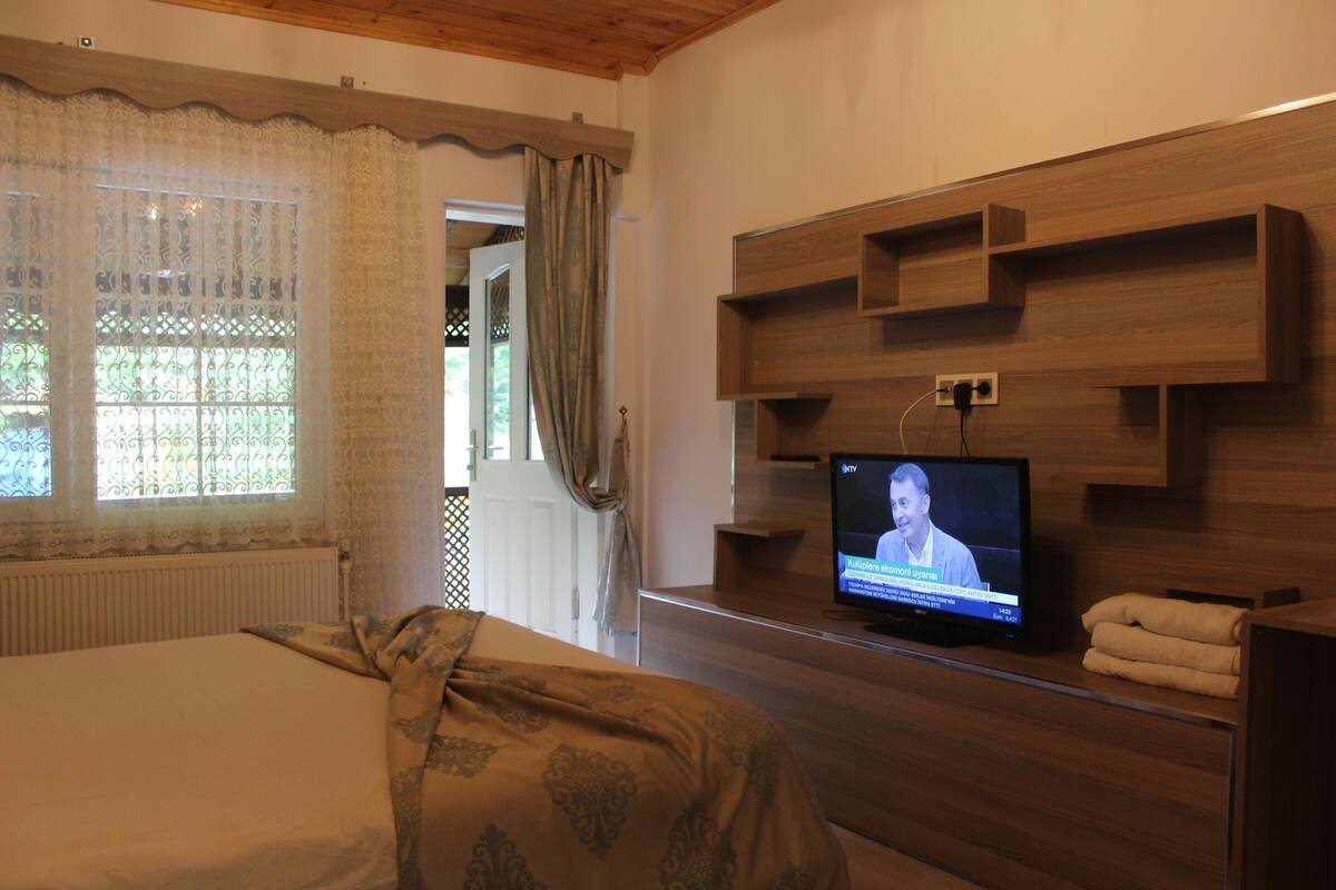 A hotel room with a bed, a TV on a wooden shelf, and a window with curtains.