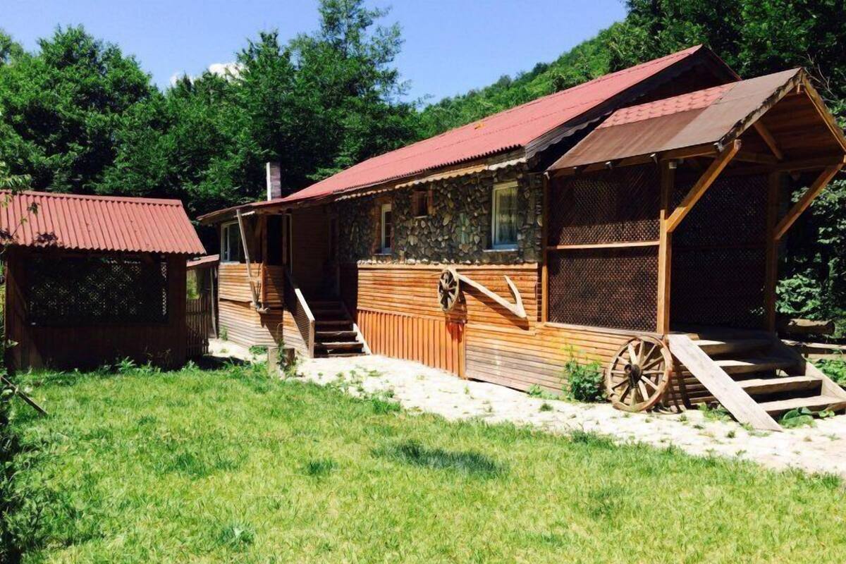 A rustic wooden cabin with a stone foundation, a wooden porch, and a large wooden wheel.