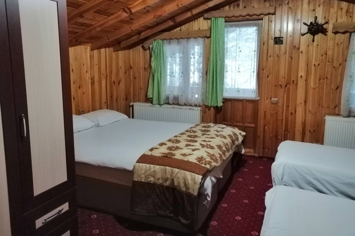 A wooden cabin room with two beds, a wardrobe, and a window with curtains.
