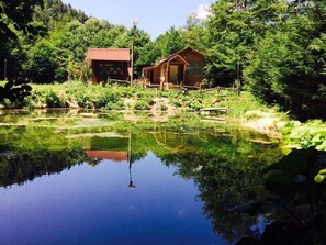 A rustic cabin with a wooden exterior, situated beside a calm pond surrounded by lush greenery. - Abant Dere Otel (Bolu)