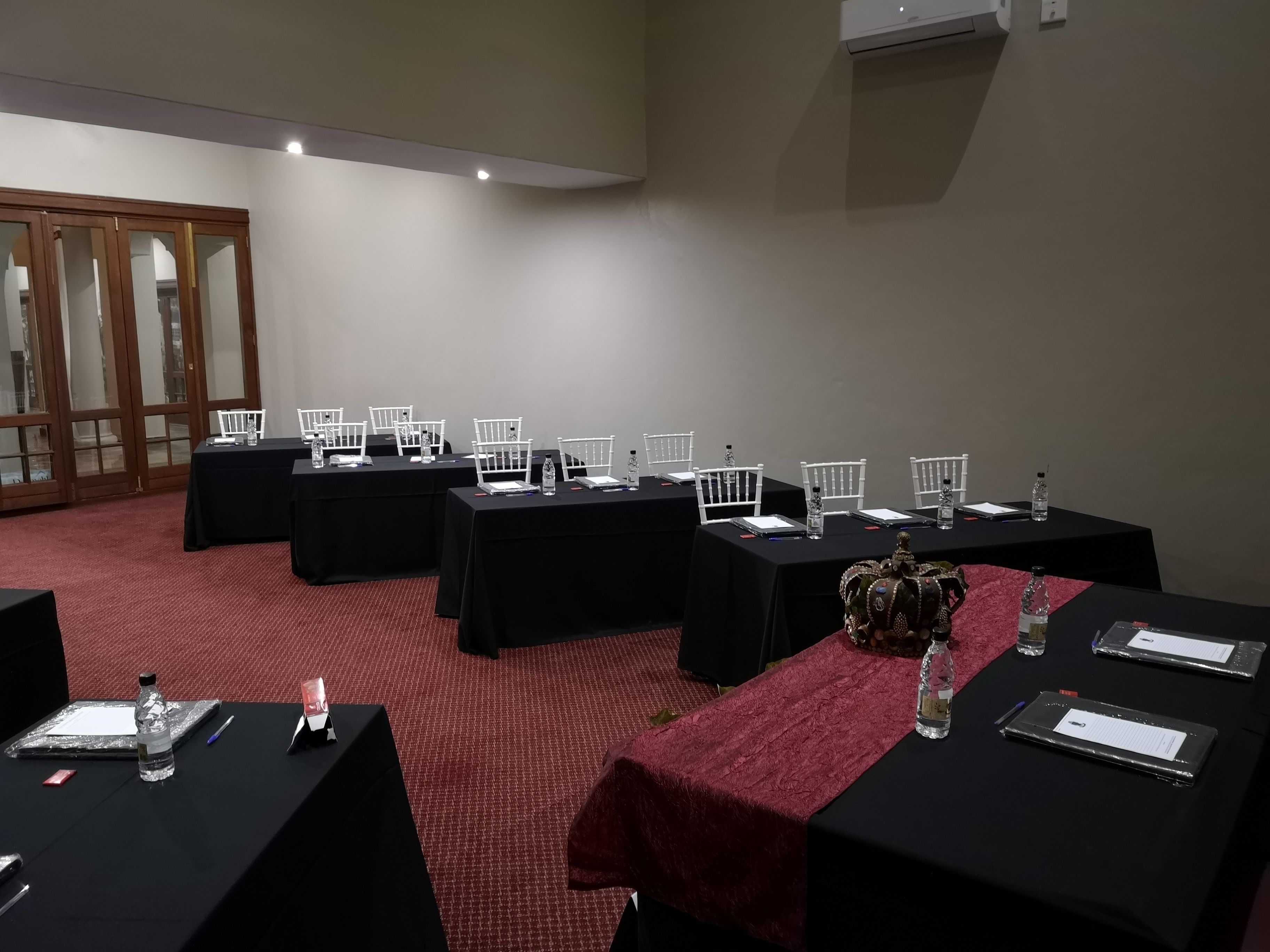 Une salle de conférence dotée de plusieurs tables, chacune étant agrémentée de chaises blanches, de nappes noires et de bouteilles d’eau.