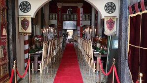 Un hall somptueux, avec un tapis rouge menant à une scène, bordée de rangées de chaises et de cordes rouges.
