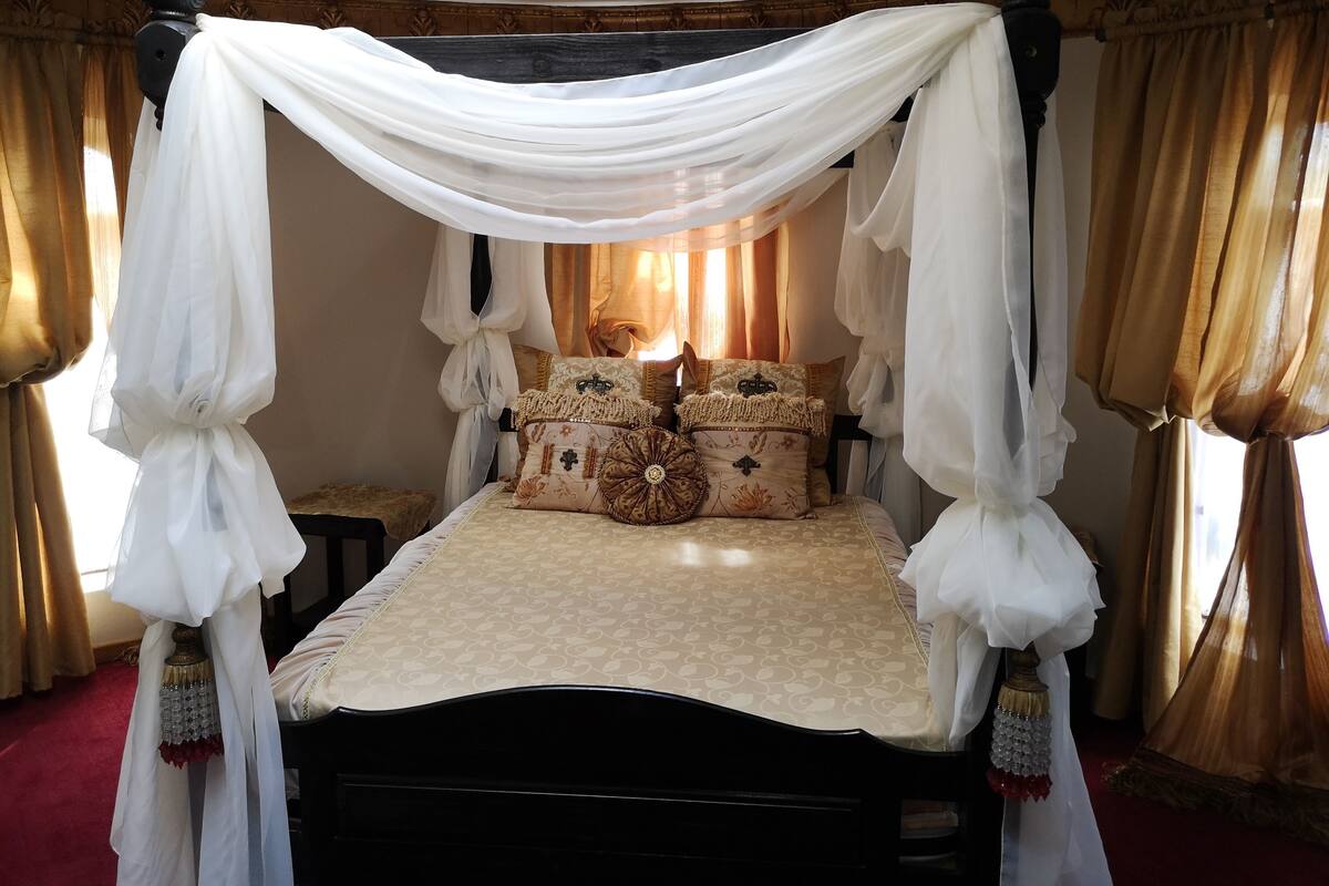 Un lit à baldaquin à quatre poteaux, avec un dais drapé au-dessus de la tête de lit, une couvre-lit à motifs et des coussins décoratifs.